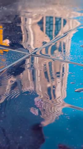 Vertical video: ornate tower reflecting and warping on rain-soaked tiles with central ripples