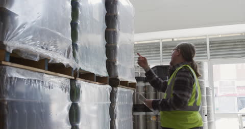 Warehouse Worker Inspecting Stacked Product Pallets