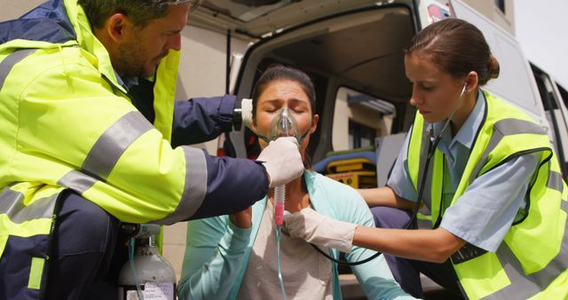Emergency medical team providing assistance to a woman wearing an oxygen mask beside an ambulance. The paramedics are focused and professional, ensuring she receives the necessary care. Ideal for use in healthcare, emergency services, first aid training materials, and public safety promotions.