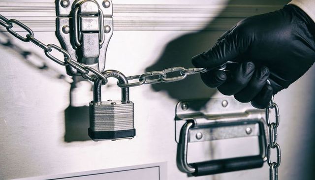 Black Gloved Hand Securing Chain and Padlock on Metal Equipment Case for Secure Transport