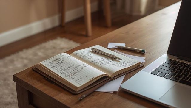 Sunlit leather journal with handwritten notes and laptop on wooden coffee table