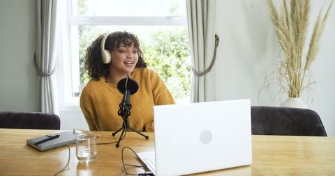 African american woman recording podcast at home with microphone, laptop and headphones