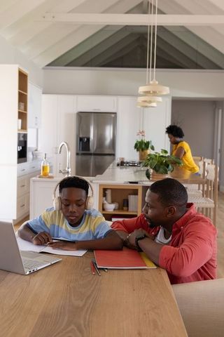 African american father helping son with remote learning on modern kitchen island