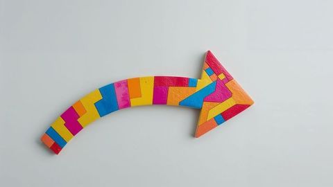 Colorful geometric curved arrow sculpture on light grey surface
