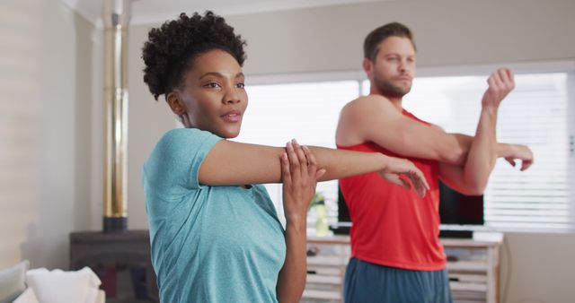 Image of focused diverse couple training together at home, stretching. Love, relationship and spending quality time together at home.