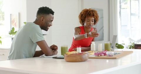 African american couple planning supplement routine in bright modern kitchen with smoothies