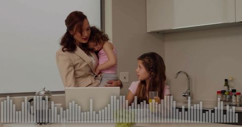 Working mother comforting toddler while older daughter drinking juice at kitchen counter