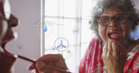 Elderly woman applying lipstick with tech elements reflection