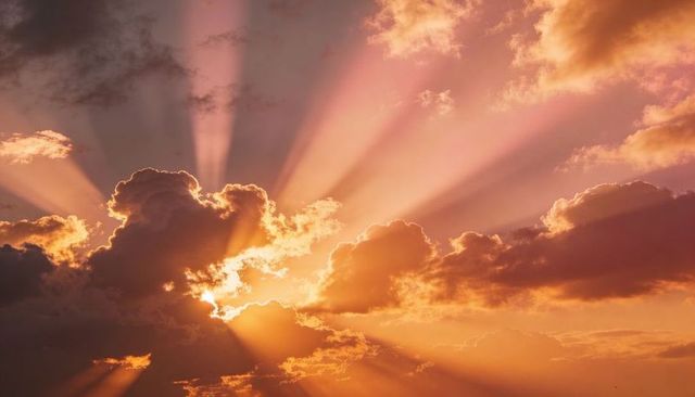 Golden Sunbeams Streaming Through Cumulus Clouds at Vibrant Sunset Skies