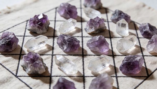 Raw amethyst clusters and clear quartz points on gridded beige cloth for crystal grid