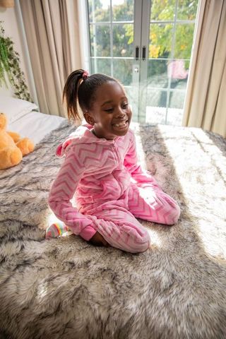 African american girl in pink chevron onesie smiling on cozy bed by sunlit french doors