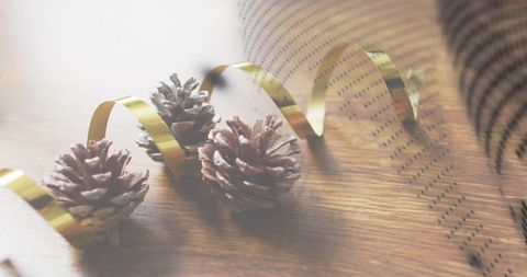 Frosted pine cones resting on warm wood with curling gold ribbon and dotted paper backdrop