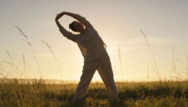 Backlit woman stretching in meadow at golden hour sunrise silhouette wearing loose linen outfit