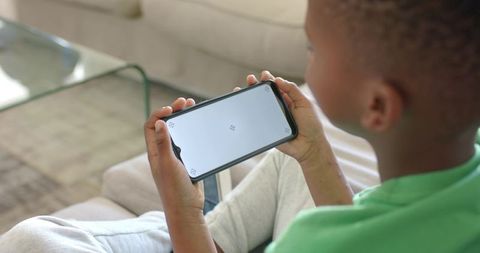 African American boy holding smartphone on couch with blank screen for app mockup