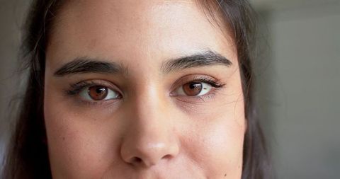 Close-up female gaze with brown eyes and subtle eyeliner, natural skin texture, mole