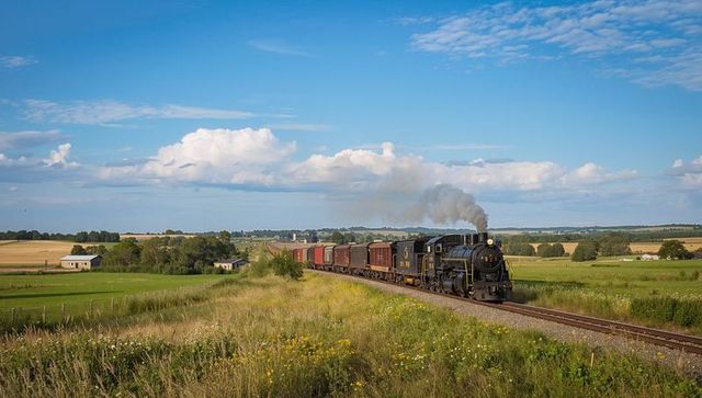 Vintage steam locomotive pulling freight train rolling through farmland under blue sky