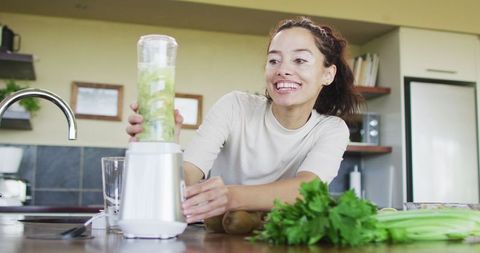 Happy Woman Blending Green Smoothie in Modern Kitchen