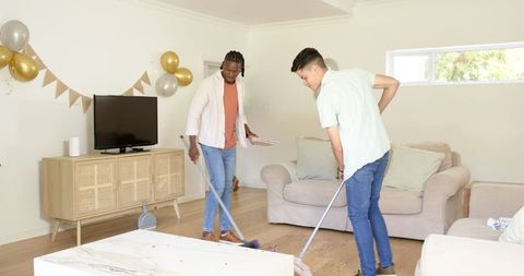 Diverse Friends Tidying Living Room After Celebration with Brooms