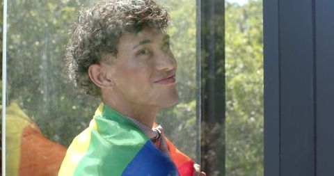 Man Embracing LGBT Pride Flag by Glass Shelter in Sunlight