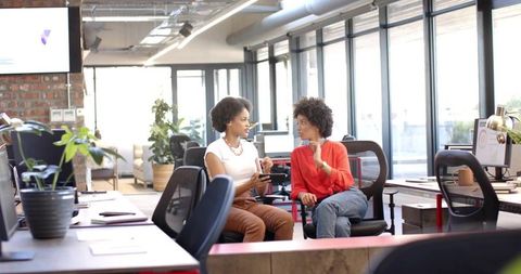 Female colleagues collaborating and sharing smartphone in modern coworkorking office