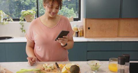 Using smartphone while preparing avocado toast on kitchen island in bright modern kitchen
