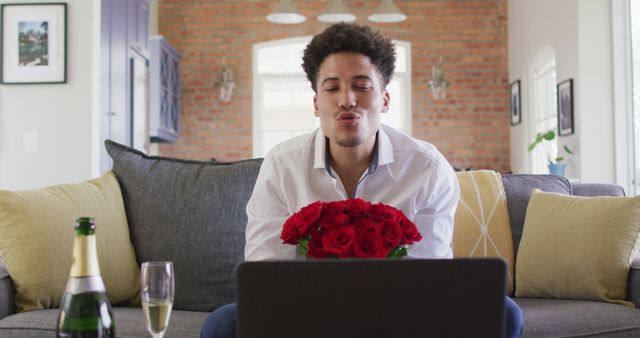 Happy biracial man with red roses making valentine's day image call on laptop. valentine's day celebration, romance and communication technology.