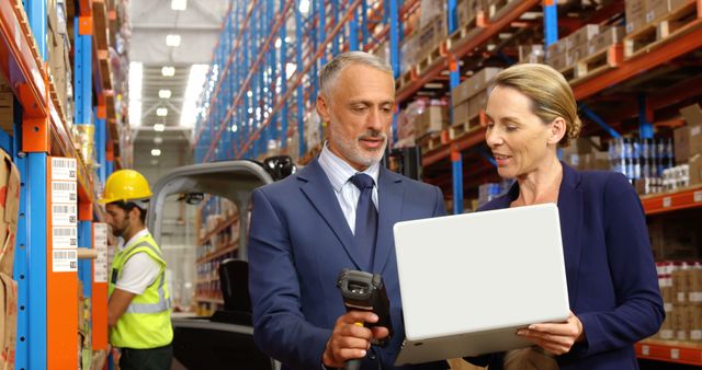 Warehouse manager holding barcode scanner and worker with laptop collaborating on inventory logistics. Worker in yellow safety vest and hard hat looking at product shelves. Can be used for themes related to warehouse management, supply chain operations, teamwork, and industrial settings.