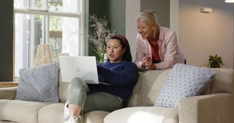 Diverse Female Friends Relaxing on Sofa Using Laptop