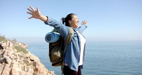 Joyful Woman Hiker on Rocky Cliff Overlooking Ocean