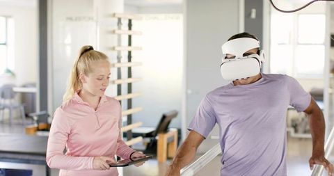 Patient using vr headset during gait therapy on parallel bars with therapist holding tablet