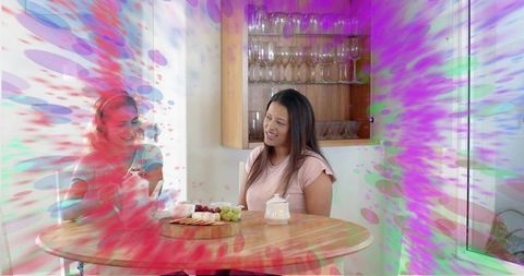 Chatting women in blue and pink sitting at round wooden table sharing cheese board
