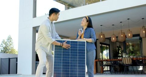 Asian couple installing solar panel on modern patio drinking water sustainable home