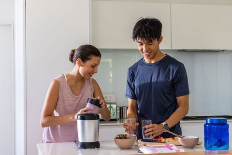 Couple preparing smoothies and fruit bowls on bright modern kitchen island for wellness