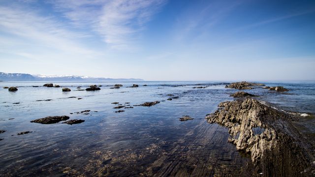 Perfect for use in travel brochures, websites about outdoor activities, or nature photography collections. Highlighting the beauty and tranquility of coastal landscapes, this image captures the serene interaction between rocky shores and the calm sea under a clear blue sky.