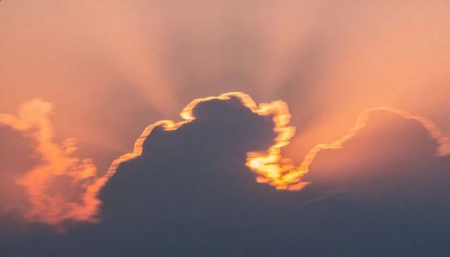 Glowing golden-rimmed cumulus cloud backlighting sunset producing crepuscular rays
