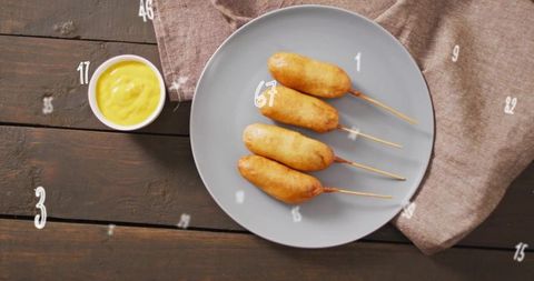 Serving four corn dogs on skewers with mustard dipping sauce on rustic wood table flatlay