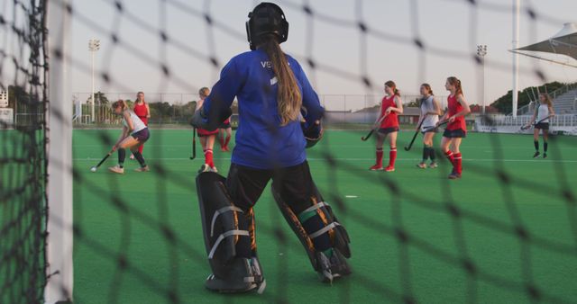 A female goalkeeper is standing in front of the goal on a soccer field in this dynamic scene. Other women players are in action, wearing uniforms and playing the game. The focus is on the skill required to defend the goal. This photo is perfect for use in articles about youth sports, promoting women's sports, teamwork, field-specific training, and goalkeeping techniques.