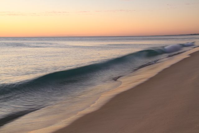 Gentle waves rolling onto a beach at sunset, with the calm ocean creating a tranquil and peaceful environment. Ideal for travel agency promotions, relaxation or stress-relief content, wallpapers, nature blogs, and social media posts to evoke a sense of calm and natural beauty.