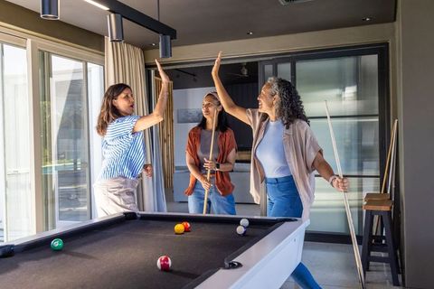 Multigenerational women high-fiving around pool table in modern home game room