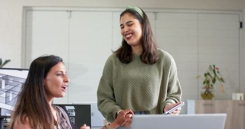 Diverse female team collaborating over architectural plans with laptop and phone in office