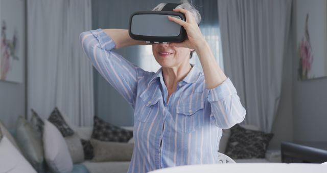 Elderly woman enjoying using a virtual reality headset at home, exploring technology and having fun. Perfect for illustrating the integration of modern technology into the lives of senior citizens, depicting new experiences and innovative lifestyle changes. Use for tech content, elderly care articles, or home environment themes.