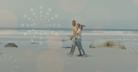 Couple strolling on sunny beach with abstract overlays