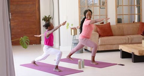 African mother and daughter practicing yoga in sunlit living room on purple mats