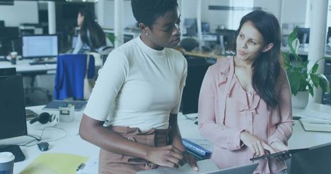 Women collaborating over laptop and tablet in modern open-plan office discussing strategy