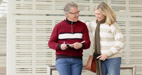 Senior couple sharing warm moment at transit concourse while planning trip with notebook