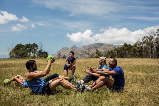 Group of fit individuals engaging in a core workout using medicine balls in an outdoor bootcamp setting. Ideal for use in fitness blogs, health and wellness websites, promotional materials for fitness programs, and social media posts promoting outdoor exercise and group fitness activities.