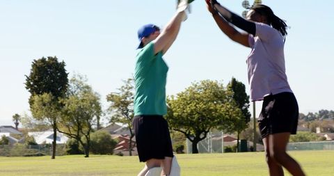 Teen cricket players celebrating wicket on local field high-fiving while resetting stumps