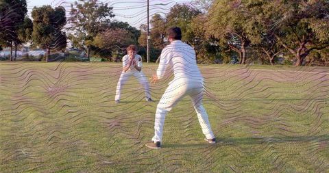 Two male cricketers practicing catching and wicketkeeping on sunlit park oval