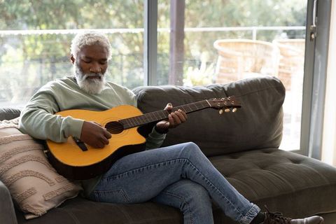 Senior african american man playing acoustic guitar on sofa in sunlit room