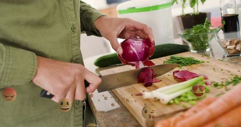 Woman slicing red onion on wooden cutting board with chef knife, scallions and vegetables